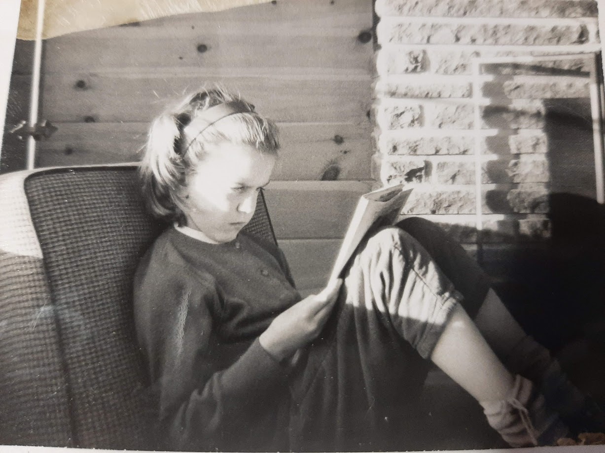 Joanne as a child, reading a book outdoors.